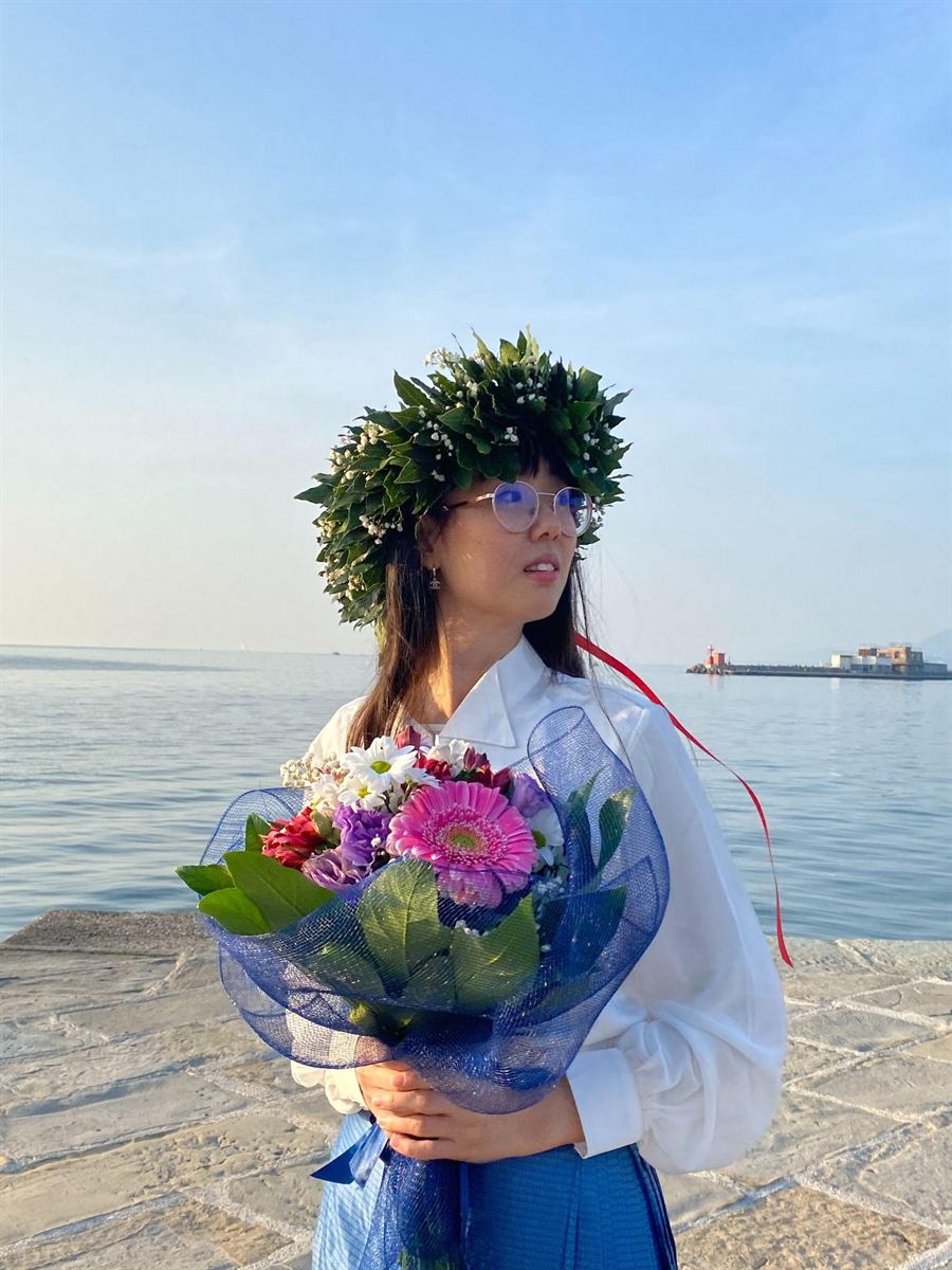 Valentina il giorno della laurea, sul lungomare, con la corona d'alloro e un mazzo di fiori.